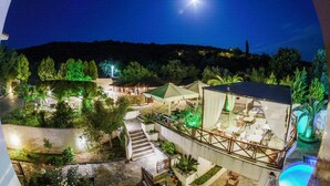 A nighttime view of a resort with outdoor seating areas, a pool, and a hill in the background. - Seralis (South Pelion)