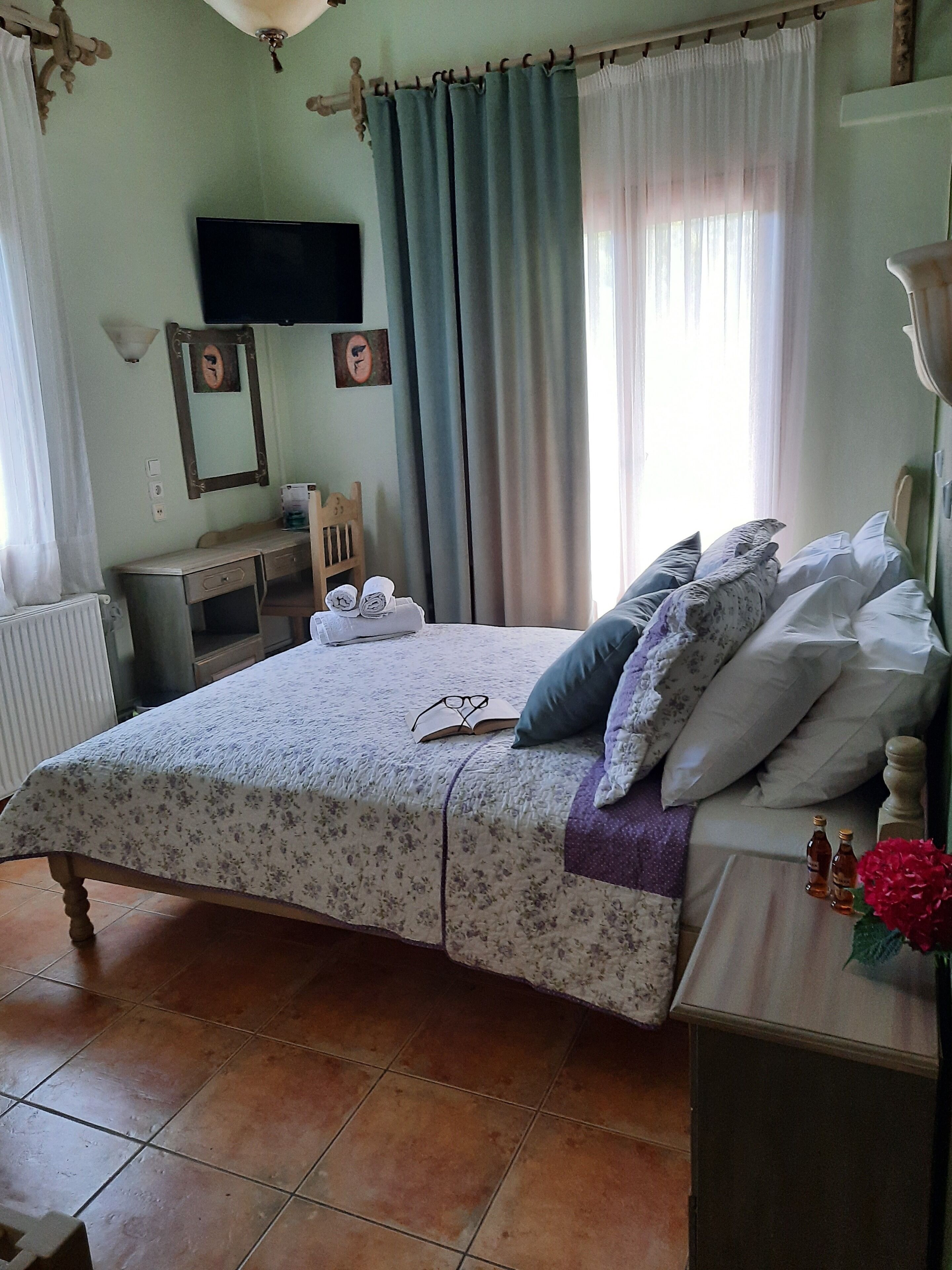 A bedroom with a bed, a desk, a chair, a television, and a window with curtains.