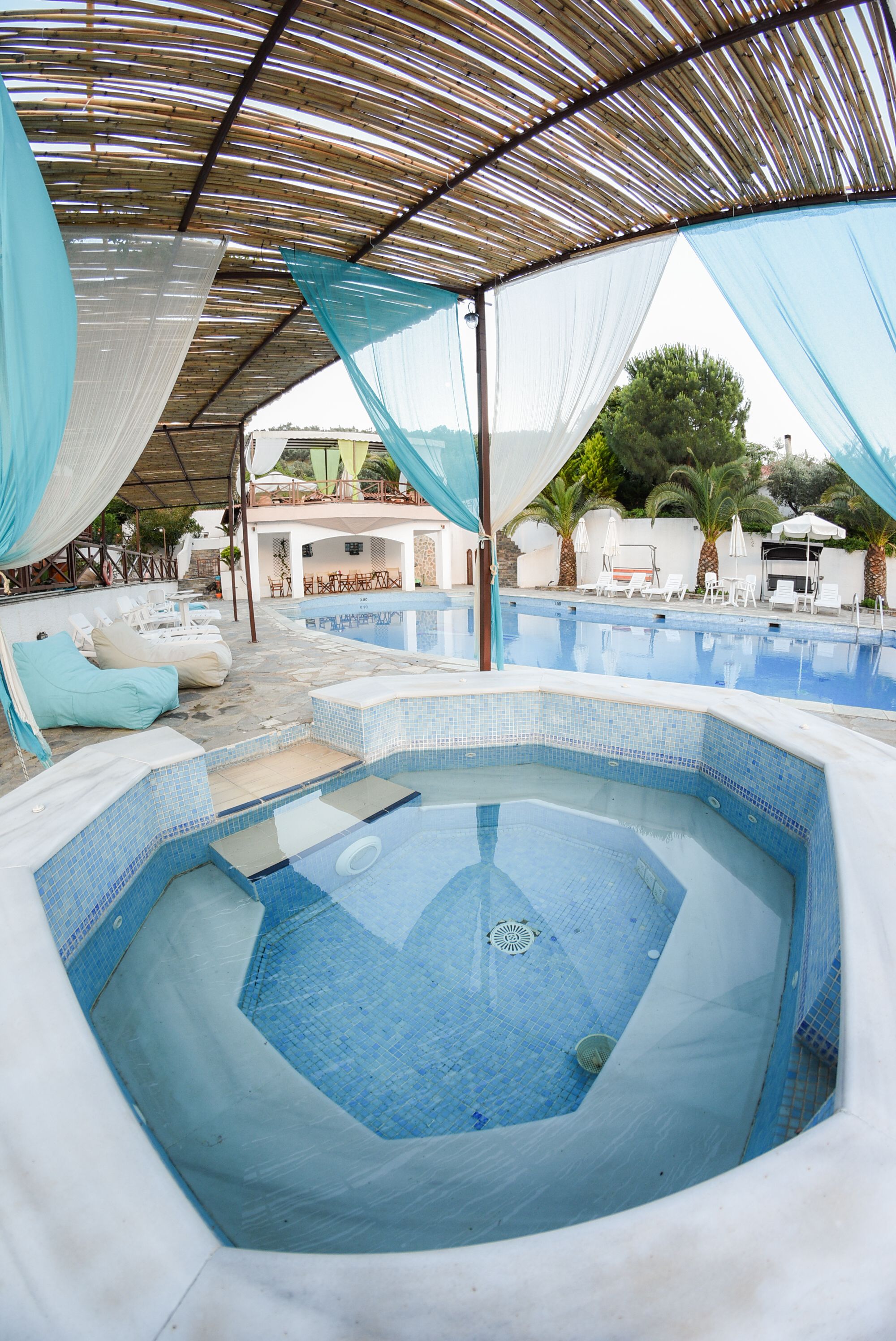 Una piscina con hidromasaje, sillas de descanso y una zona cubierta con vistas al paisaje.