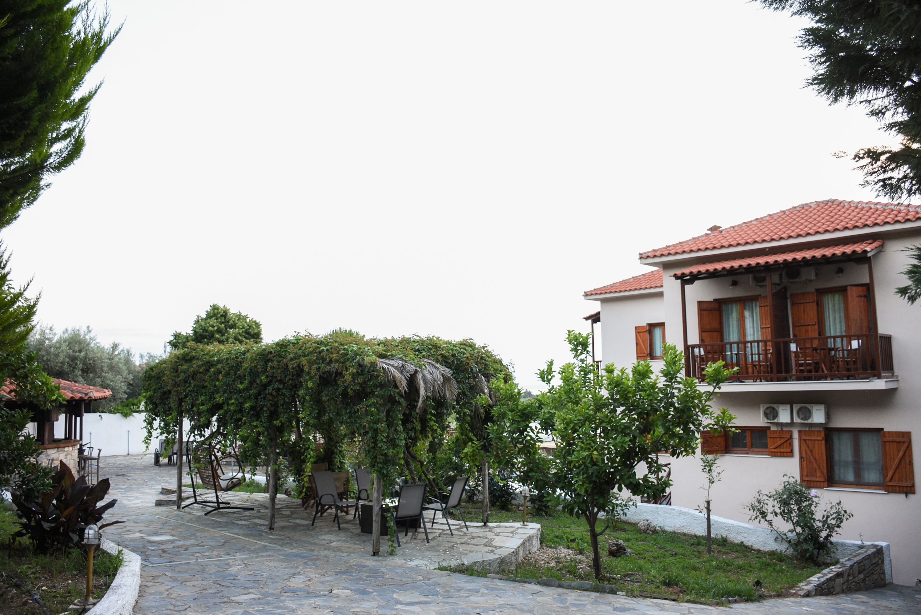 Un patio con suelo de piedra, mobiliario exterior y un edificio con tejado de tejas rojas y contraventanas de madera.