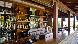 A bar with wooden shelves stocked with various liquor bottles, a stone counter, and several chairs. - Seralis (South Pelion)