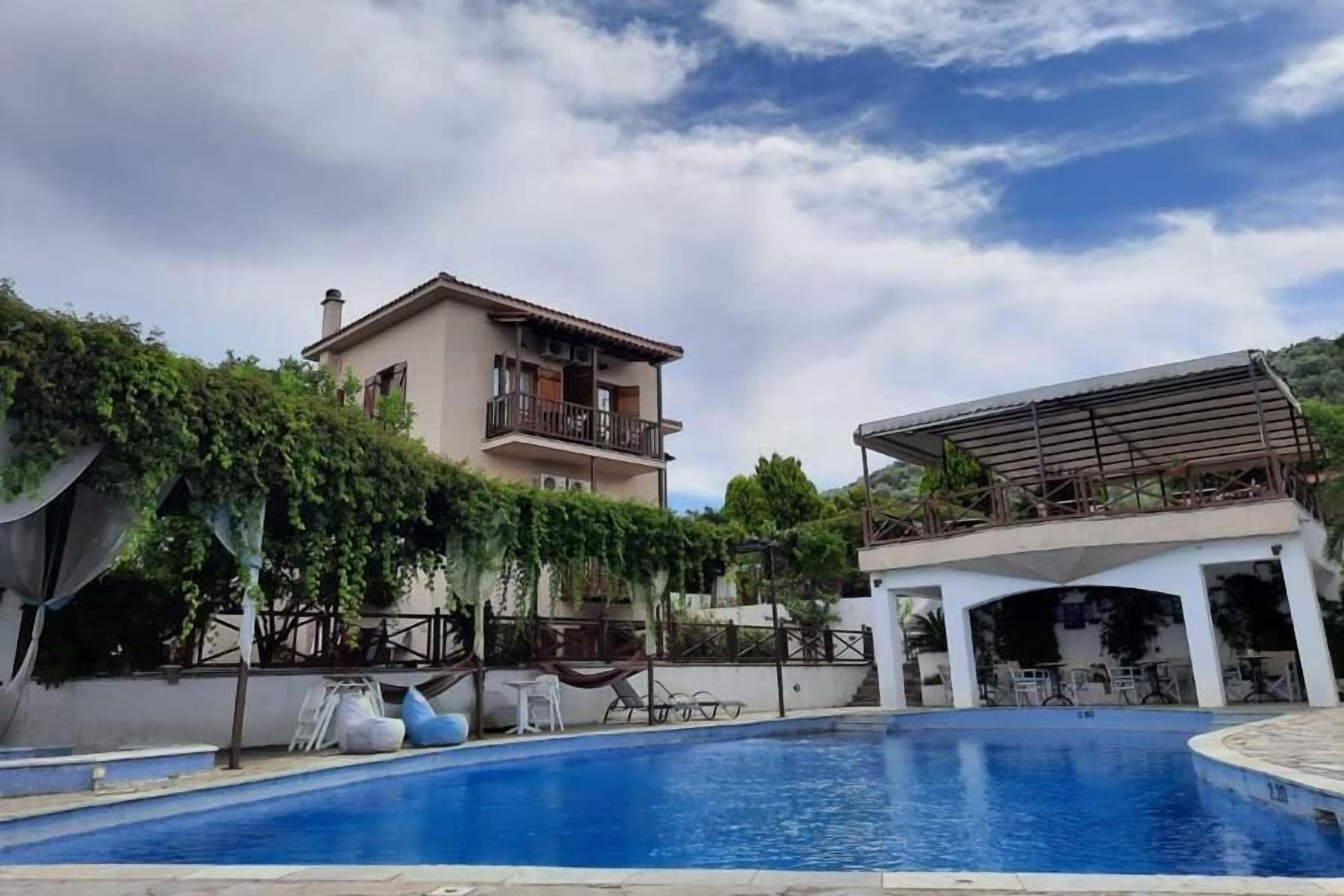 A swimming pool with a covered area, a two-story building with a balcony, and lush greenery.