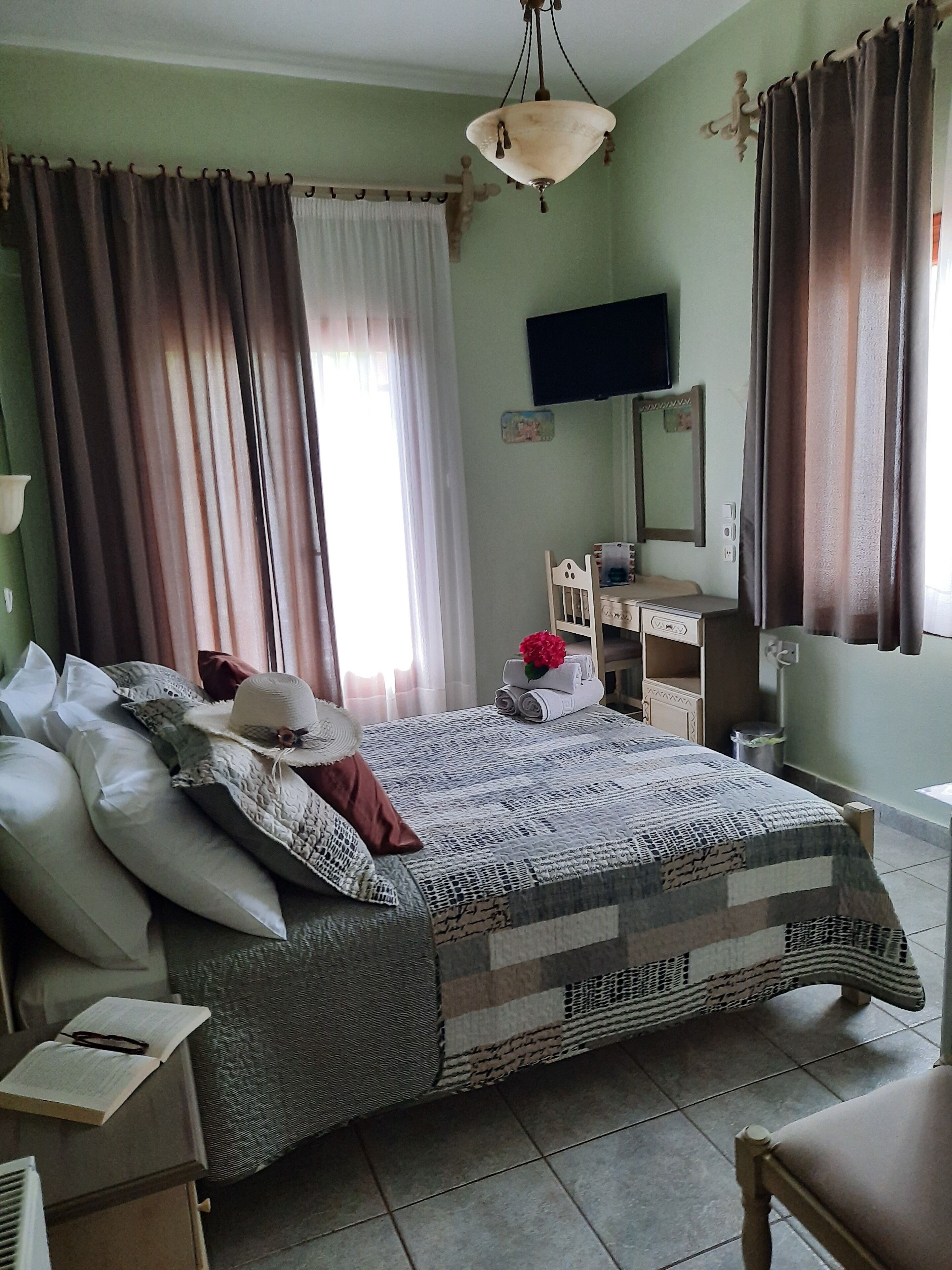 A neatly arranged bedroom with a bed, bedside tables, a dresser, and a television on the wall.