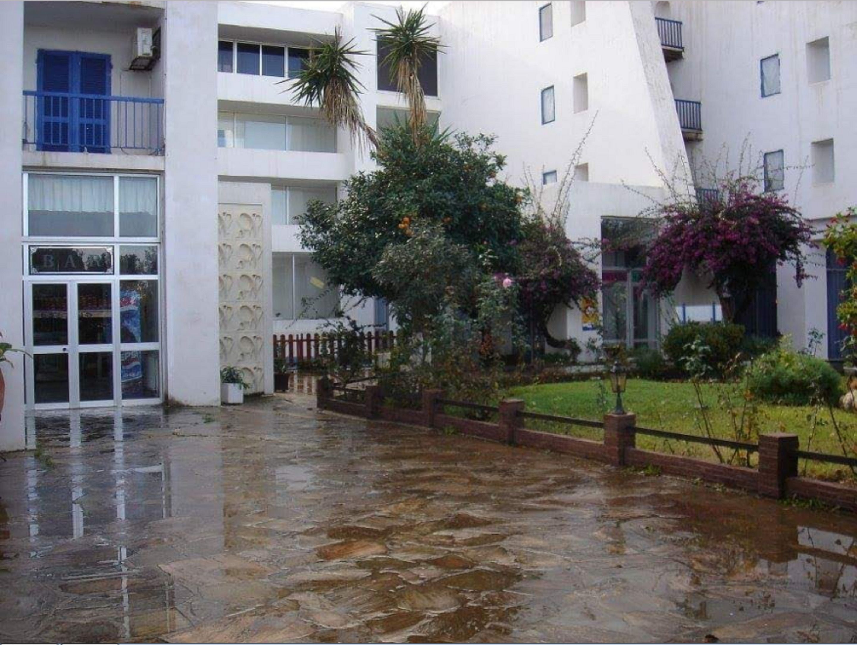 A multi-story building with a wet ground, a visible bar entrance, and a fenced garden area.