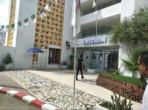 A hotel entrance with a tiled walkway, a potted plant, and a man walking towards the entrance.