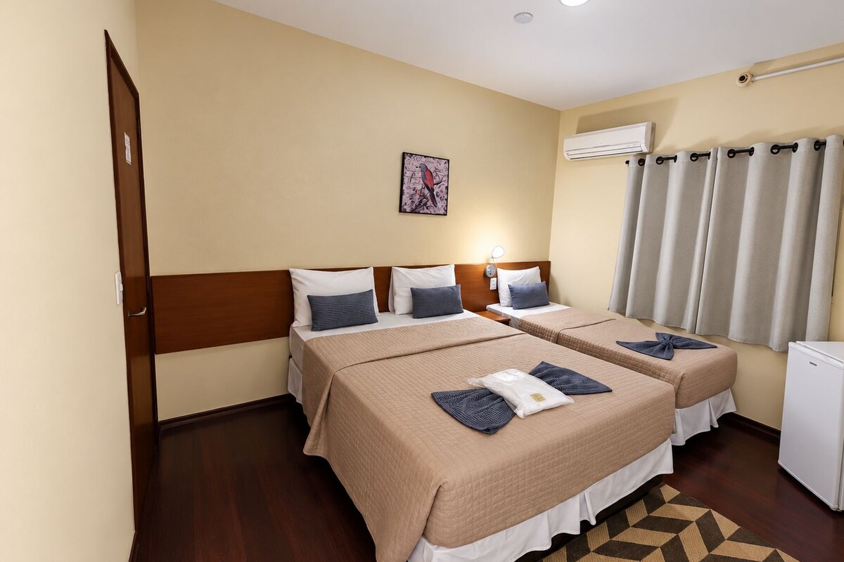 Habitación de hotel con dos camas, un refrigerador blanco pequeño, un equipo de aire acondicionado y una alfombra estampada.