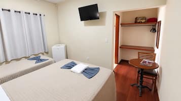A hotel room with two beds, a television, a small table with a chair, and a shelf with personal items.