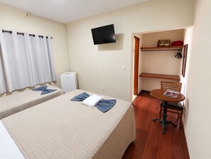 A hotel room with two beds, a television, a small table with a chair, and a shelf with personal items. - Hotel Rafeli (Boituva)