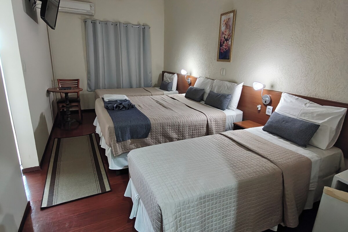 A hotel room with two beds, a small table, a chair, a desk, and a television mounted on the wall.