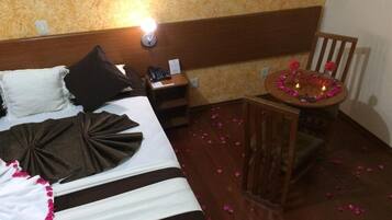 Quarto de hotel com cama, mesa de cabeceira e uma pequena mesa redonda adornada com velas e flores.