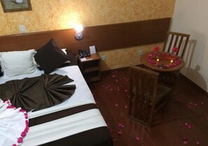 A hotel room with a bed, bedside table, and a small round table with candles and flowers.