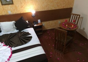 Una habitación de hotel con cama, mesita de noche y una pequeña mesa redonda con velas y flores.