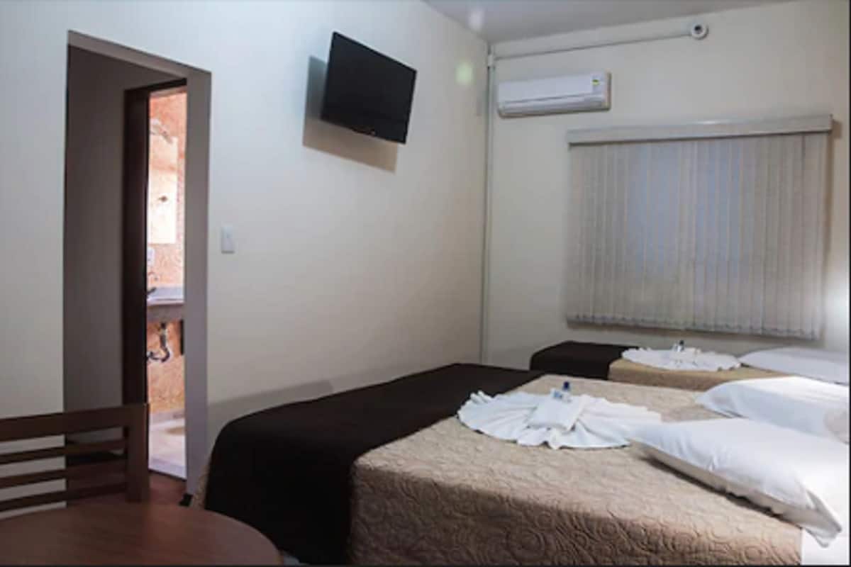 Una habitación de hotel con dos camas, un televisor montado en la pared y un equipo de aire acondicionado.
