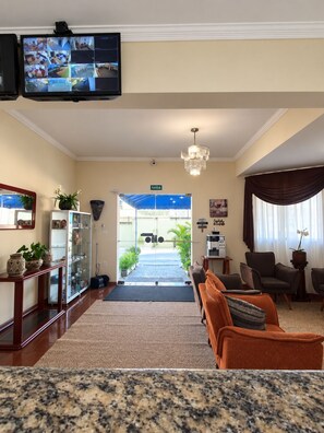 Vestíbulo de hotel con televisión montada en la pared, mostrador de recepción, zona de estar y vistas al área exterior.