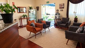 A hotel lobby with a reception desk, seating area with armchairs, a chandelier, and a coffee machine.