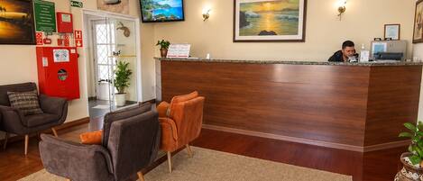 A hotel lobby with a reception desk, seating area, and a television screen.