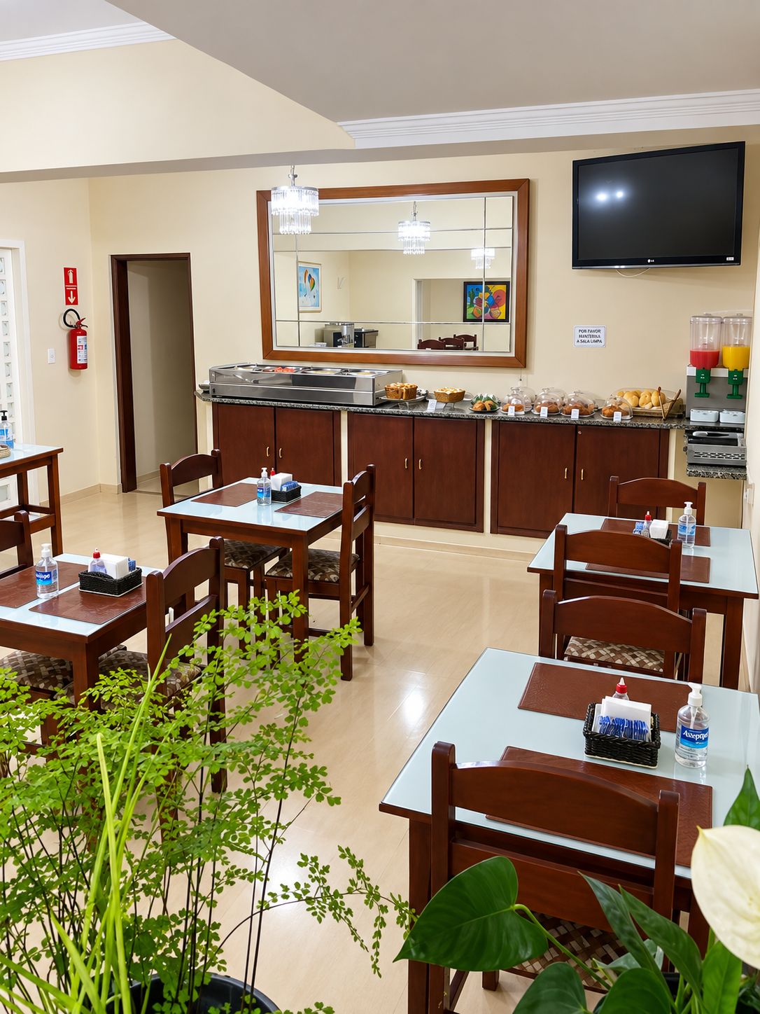 A hotel dining area with tables, chairs, a buffet counter, a television, and a fire extinguisher.