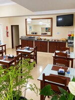 Comedor de hotel con mesas, sillas, mostrador de buffet, televisor y extintor.