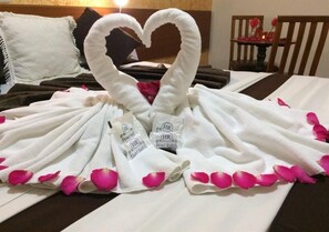 Ein Bett mit weißen Handtüchern, die zu einem Herz geformt sind, einige mit Branding des Hotel Rafael, und rosa Blütenblättern am Rand.