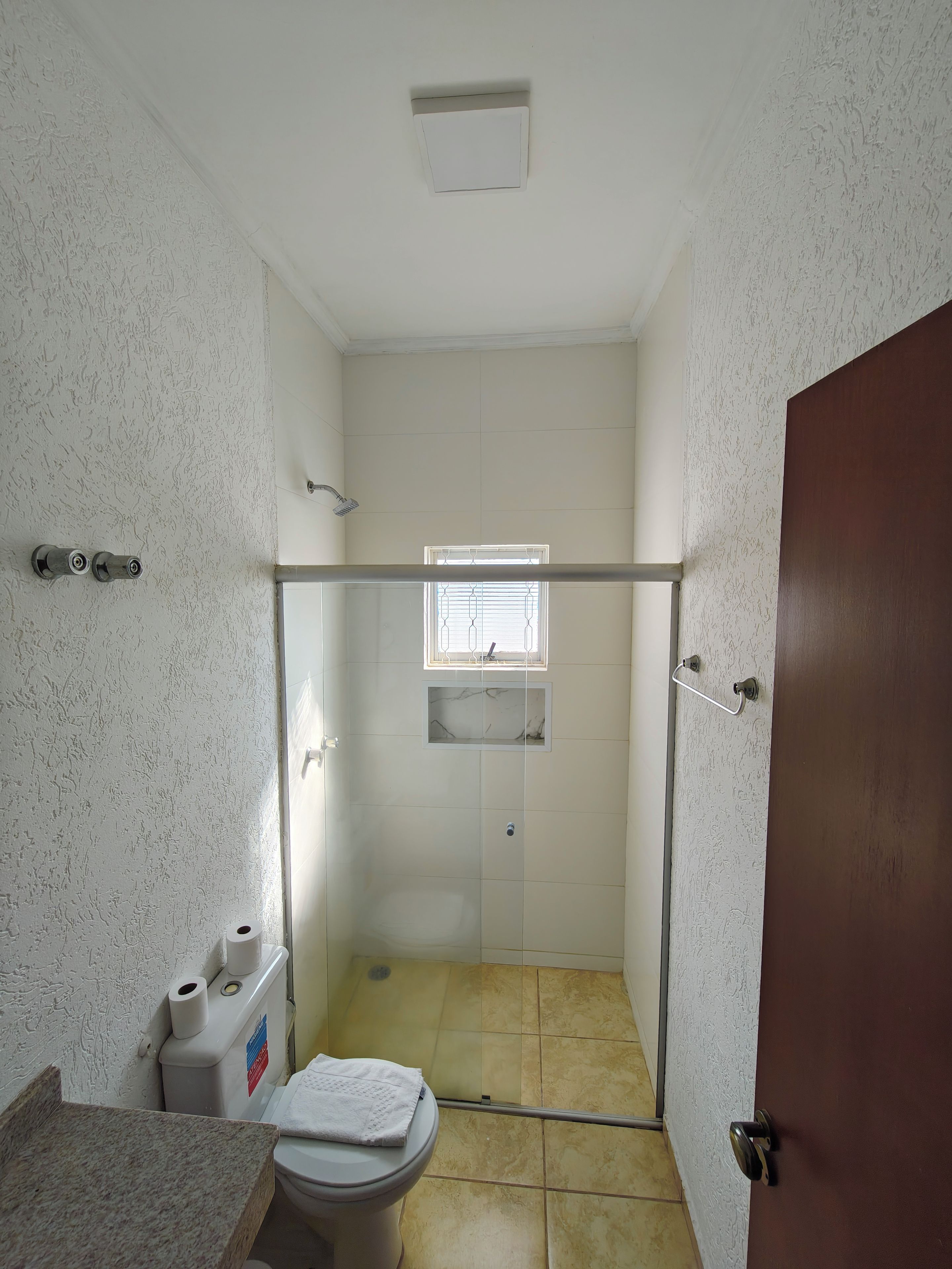 Um pequeno espaço de chuveiro fechado, com porta de vidro, vaso sanitário e pia com bancada de mármore.