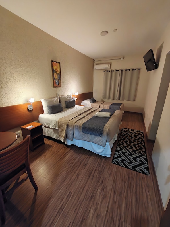 A hotel room with a bed, bedside tables, a desk, a chair, a TV, and a window with curtains.