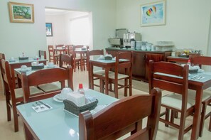 A dining area with multiple tables and chairs, a coffee station, and framed artwork on the walls.