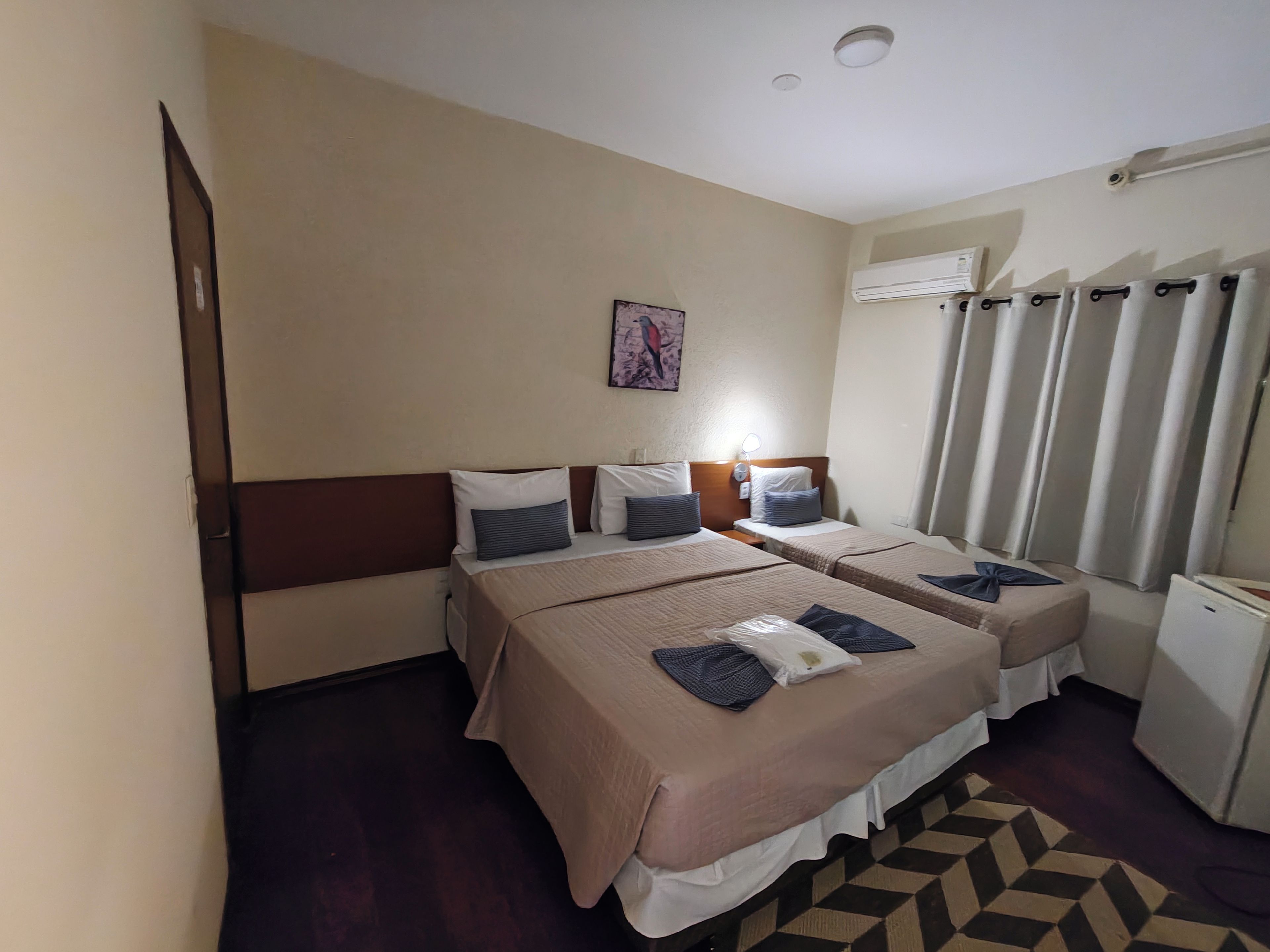 A hotel room with two beds, a small desk, a nightstand, a wall-mounted air conditioner, and a patterned rug.