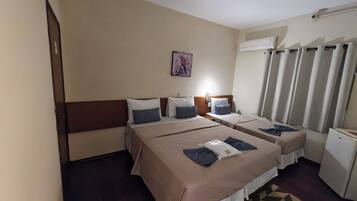 A hotel room with two beds, a small desk, a nightstand, a wall-mounted air conditioner, and a patterned rug.