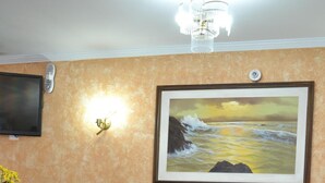 A reception area with a wooden reception desk, a framed painting of a seascape, a wall-mounted light fixture, and a television on the wall. - Hotel Rafeli (Boituva)
