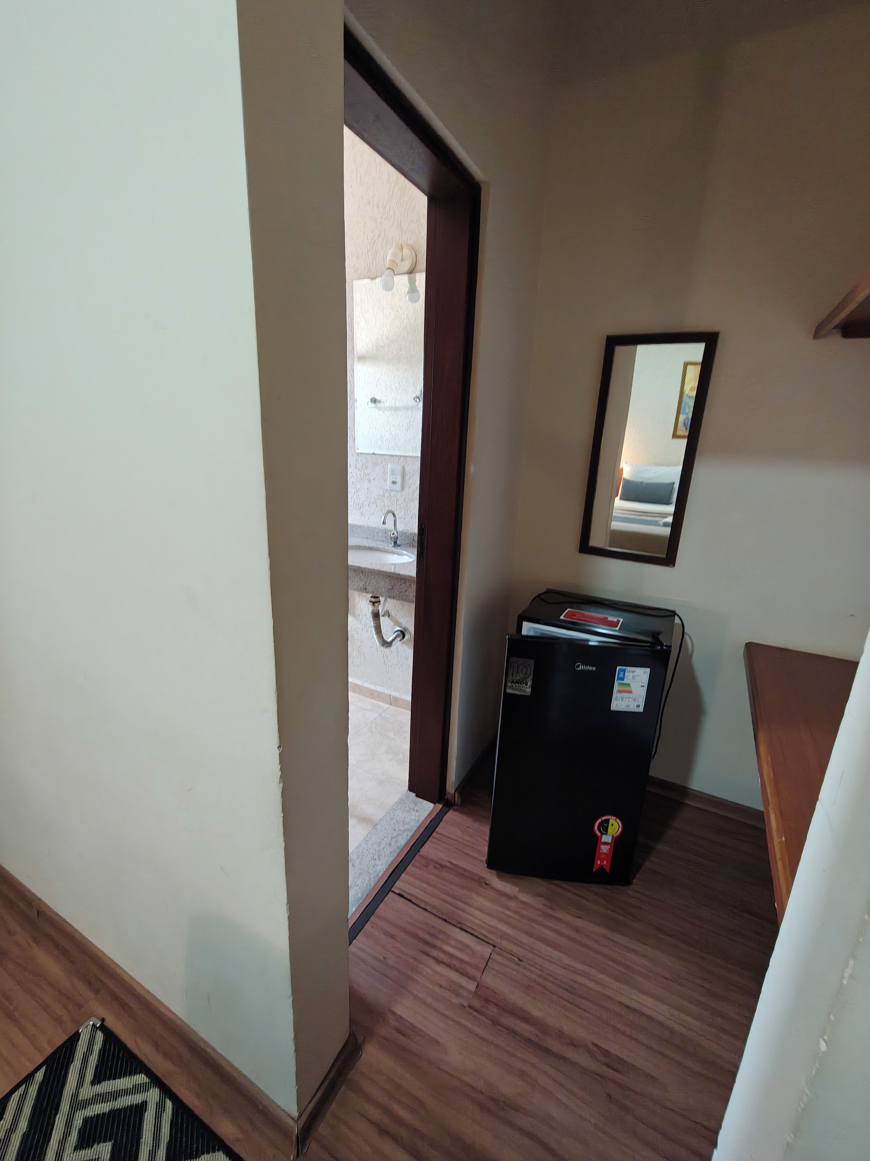 A room with a refrigerator, a mirror, and a door leading to an outdoor area.