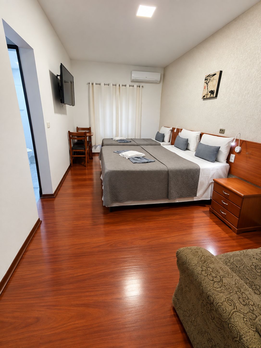 Une chambre d’hôtel avec deux lits, une commode en bois, une télévision et un tableau au mur.
