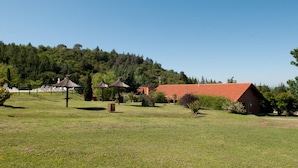 A rural setting with a red-roofed building, thatched-roof structures, and a grassy field. - Green House (Villa General Belgrano)