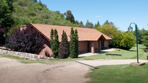A small brick building with a tiled roof, surrounded by a well-maintained lawn and trees. - Green House (Villa General Belgrano)