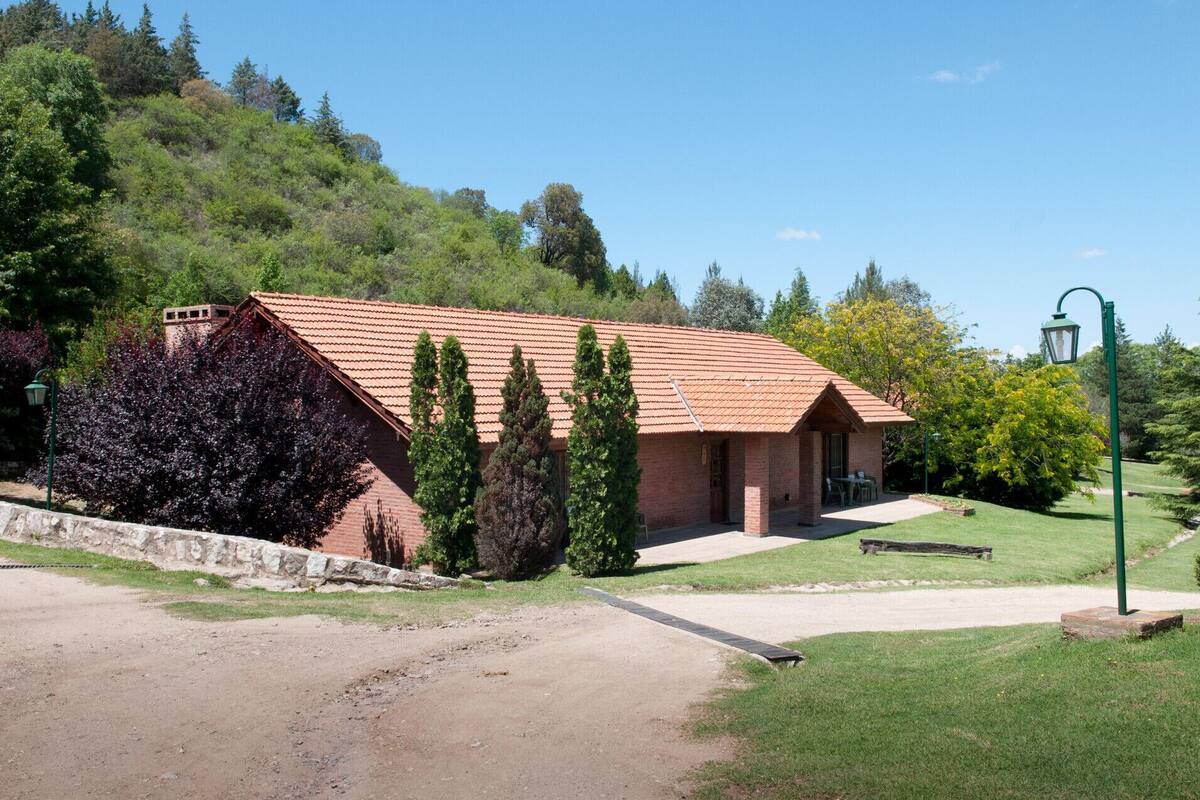 A small brick building with a tiled roof, surrounded by a well-maintained lawn and trees.
