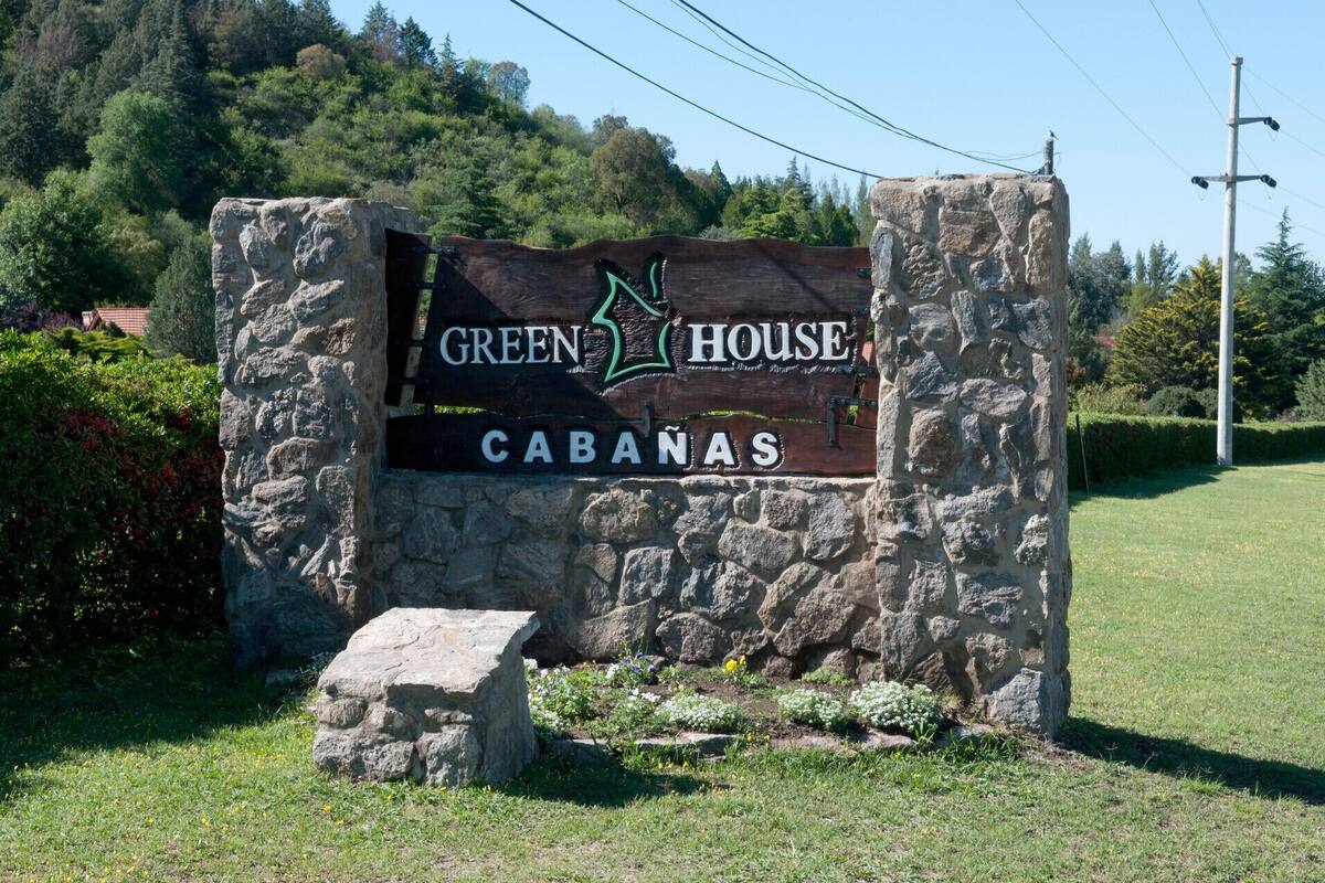 A sign for 'Green House Cabanas' with a stone structure and a grassy area in the foreground.