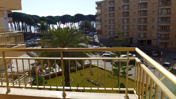 Un edificio residenziale con diversi balconi, un'area di parcheggio con auto e uno spazio verde con palme.