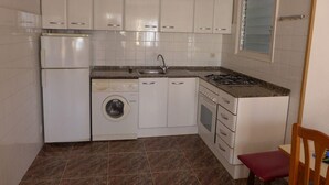 Una cucina compatta con mobili bianchi, una lavatrice, un lavandino e un fornello.