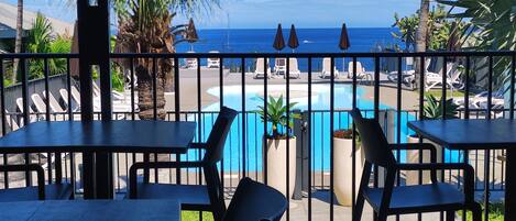 Un espace aménagé au bord de la piscine avec des tables et des chaises, une vue sur l’océan, ainsi que des chaises longues et des parasols.