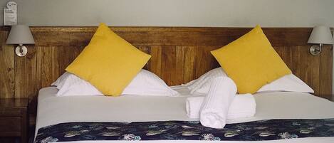 A neatly made bed with white and yellow pillows, a floral bedspread, and a wooden headboard.