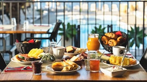 Un bufé de desayuno con diversos platos, un bol de fruta y vistas a la piscina.
