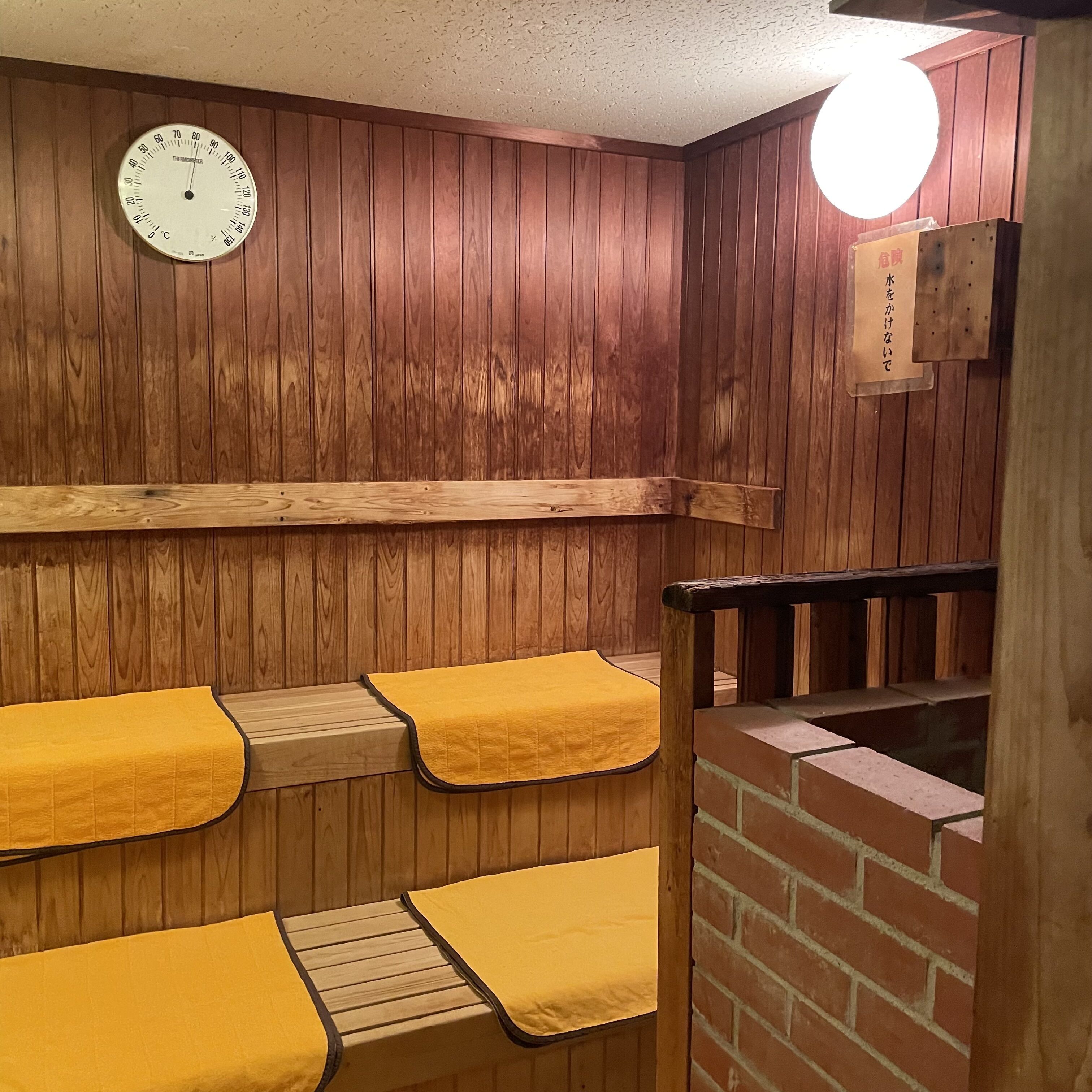 A sauna room with wooden walls, a thermometer, and benches with yellow towels.