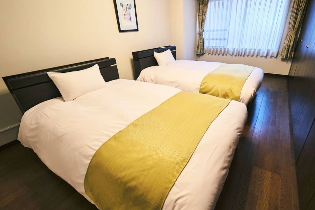 A hotel room with two beds, a wooden floor, and a door.