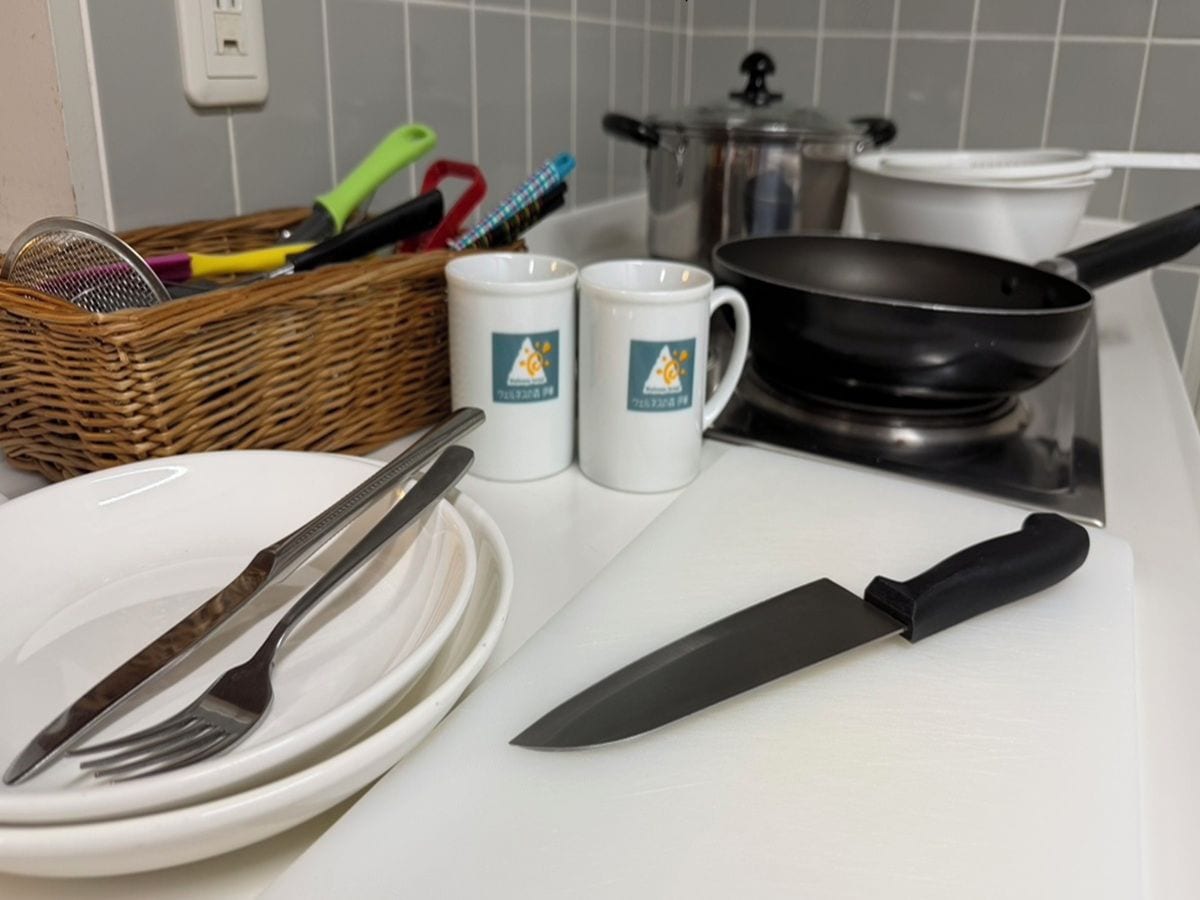 Un plan de travail de cuisine avec une planche à découper, un couteau, une poêle et un panier contenant des ustensiles.