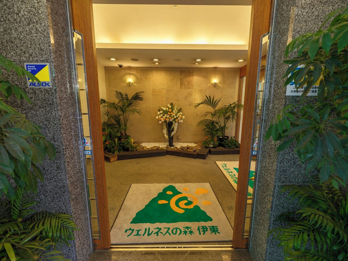 A hotel entrance with a reception desk, a flower arrangement, and a carpet with a logo.