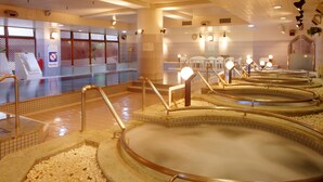 Una tradizionale onsen giapponese con diverse vasche termali, pavimento in legno e pareti piastrellate.