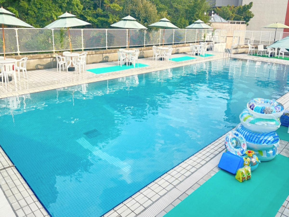 A swimming pool with lounge chairs and umbrellas, surrounded by a fence.