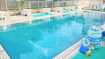 A swimming pool with lounge chairs and umbrellas, surrounded by a fence.