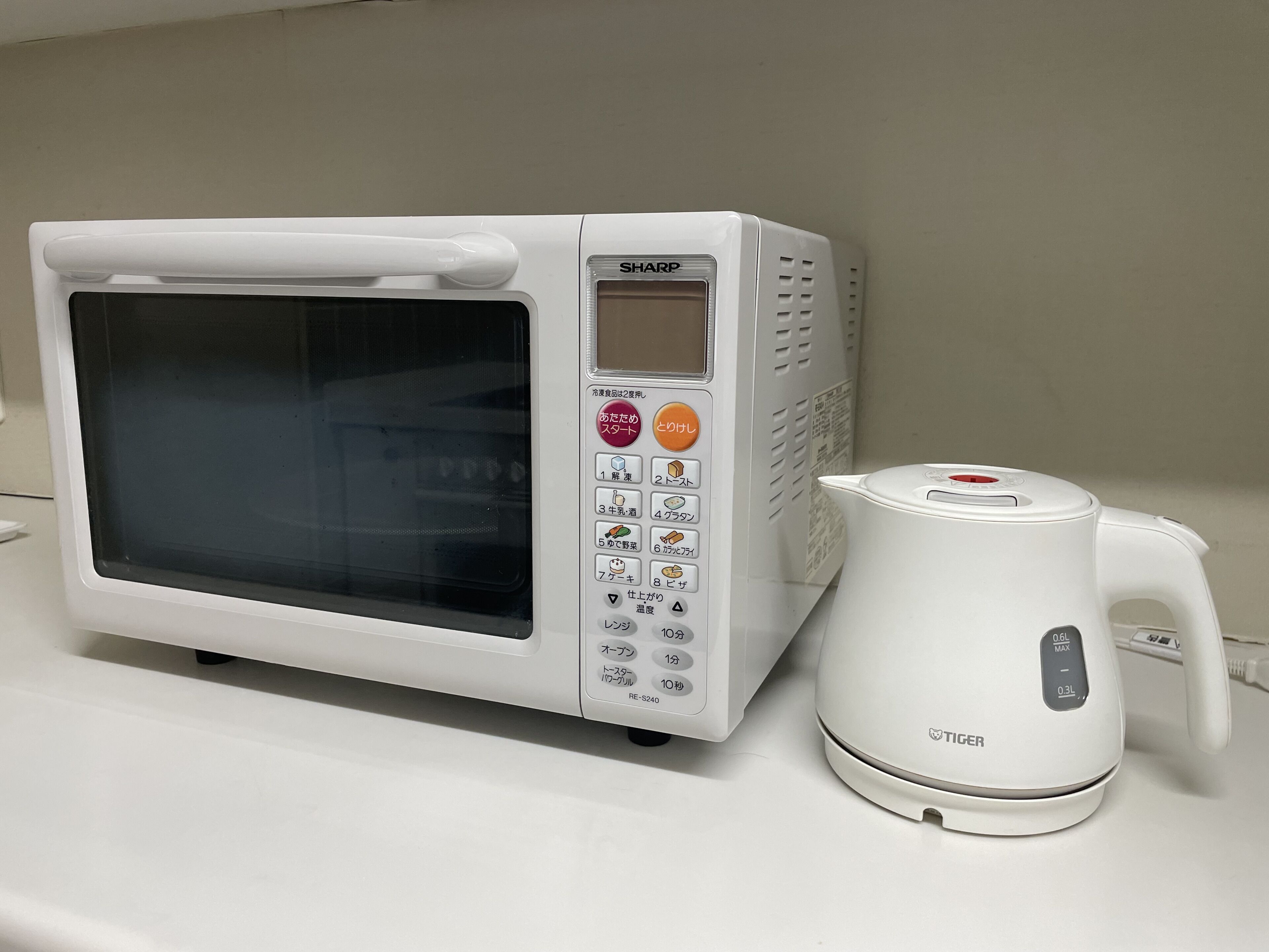 Un horno microondas blanco Sharp con pantalla digital y panel de control, junto a una tetera eléctrica blanca con cable de alimentación.