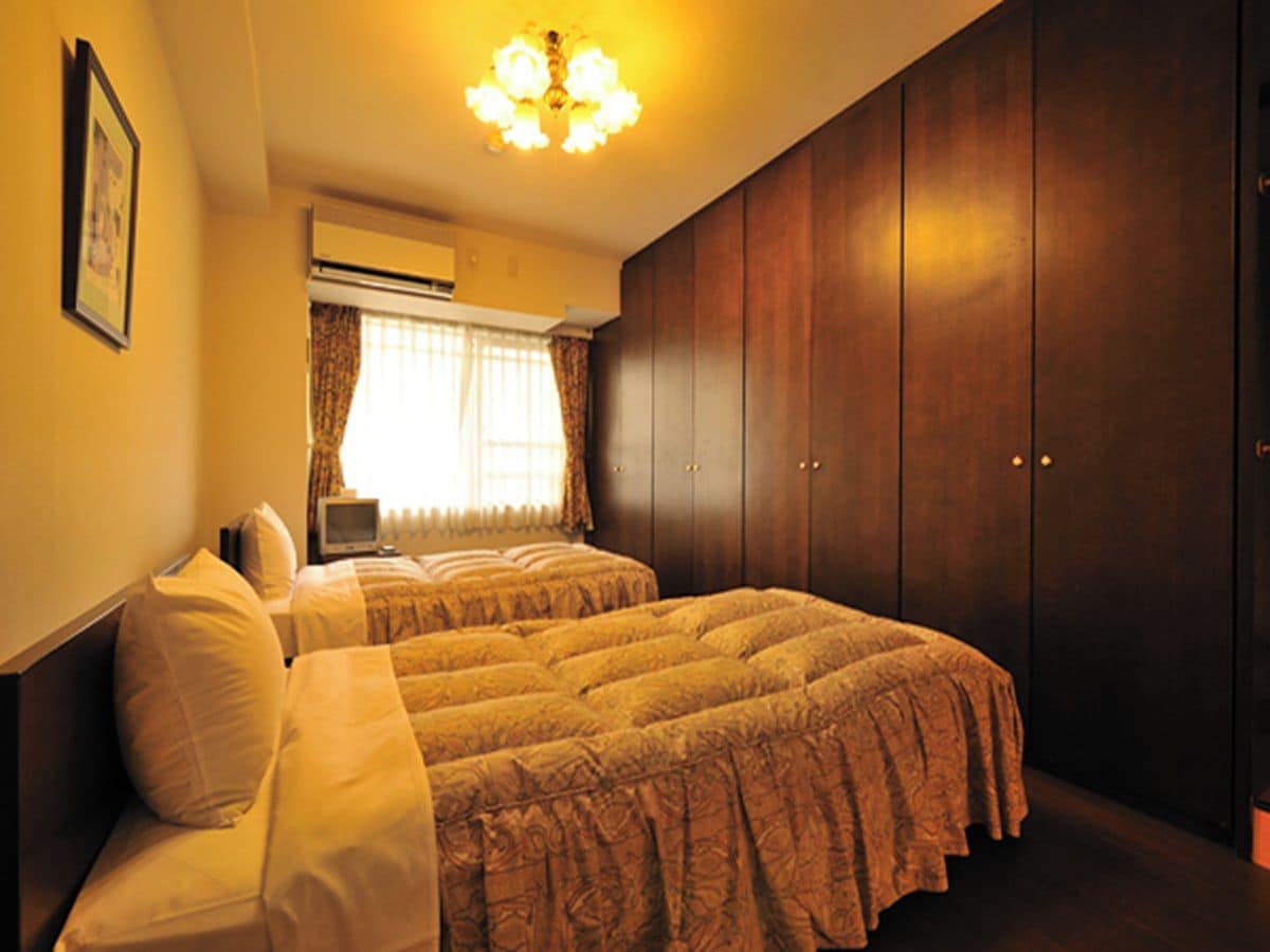 A bedroom with two beds, a wardrobe, and a television.