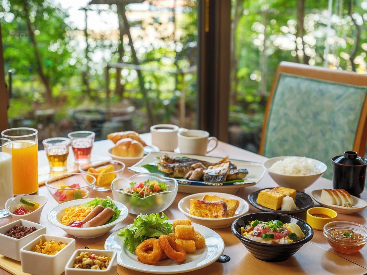 A dining table with various dishes and drinks, set in a room with a view of greenery outside.